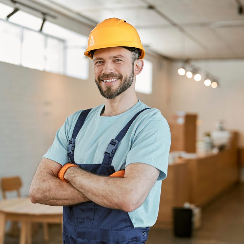 Joyful man construction worker looking at camera and smiling while keeping arms crossed